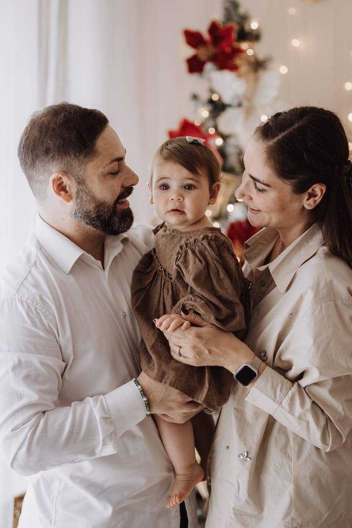 Mamma e papà abbracciano la loro bambina davanti all'albero di Natale, durante una mini sessione in studio