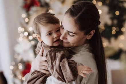 Mamma che stringe a sé la sua bambina davanti alle luci dell'albero