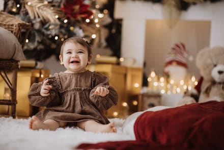 Bambina sorridente seduta nel set natalizio tra pacchi dorati e coperta rossa