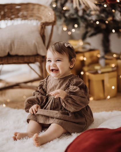 Bambina che ride seduta sul tappeto bianco del set natalizio